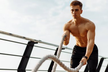 İskelede spor yapmak için antrenman ipleri kullanan kaslı fitness adamı, dövüş ipleriyle egzersiz yapan sporcu, spor konsepti, sağlıklı yaşam tarzı.