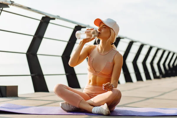 Young woman with fit body resting after intense exercise outdoors, Woman resting after workout and drinking water