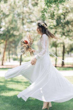 Kafasında çelenkle şık bir gelinlik içinde güzel bir gelin, göz kamaştırıcı genç bir gelin inanılmaz derecede mutlu, düğün günü. Parktaki gelinin güzel portresi.