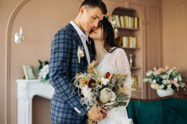 Mutlu gelin ve damat elinde bir buket düğün çiçeği, mutlu genç çift, mutlu düğün günü, gelin ve damat stüdyoda birbirlerine poz verip bakıyorlar.