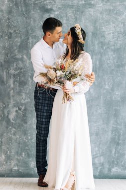 Stüdyoda yeni evlilerin fotoğraf çekimi mutlu genç çift gelin ve damadın izole edilmiş gri renkli duvar arkaplanında birbirlerine bakması boho tarzında düğün günü.