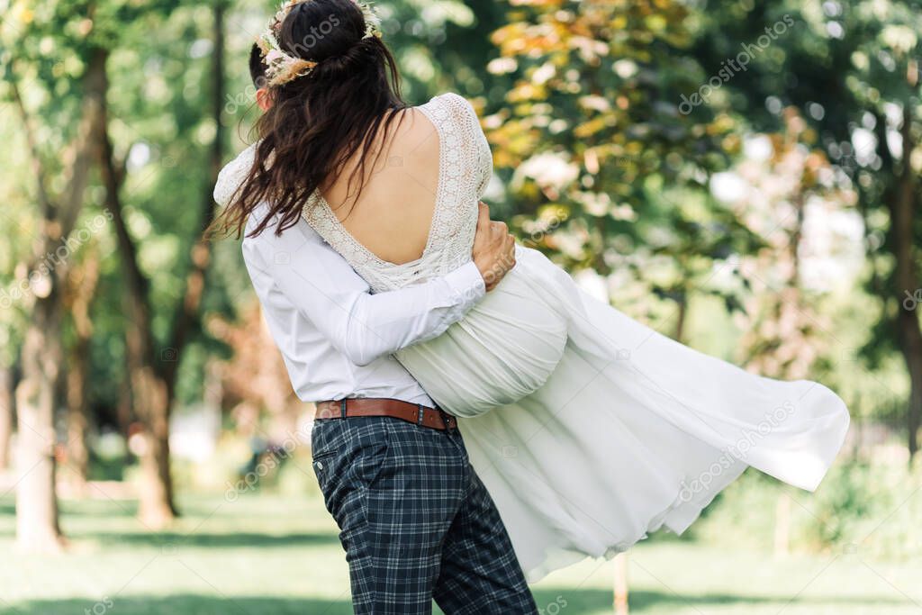 Happy wedding couple, the groom admires the happy bride, holds the bride in his arms and whirls her, in the park on a summer sunny day, happy wedding day