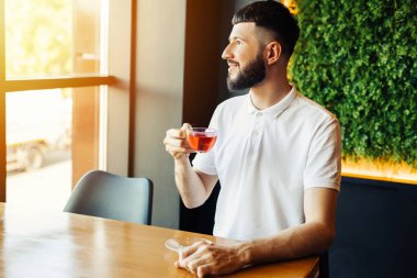 Genç, yakışıklı, sakallı, kahve molasında aromatik çay içen genç bir iş adamı.