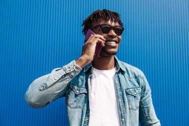 Siyah Afrikalı bir adam, telefonda konuşuyor, mavi bir binanın arka planında, ve başarı konsepti, telefonu olan bir öğrenci.