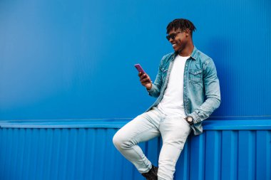 Mavi arka planda mesaj yazan Afrikalı bir adam, 5G internet konsepti, telefondaki yüksek hızlı internet, mavi çuvallı siyah adam, ve kot pantolon.