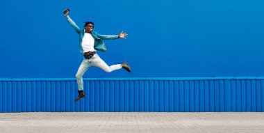 Afrikalı bir adam elinde telefonla şehirde mavi bir binanın arka planına atlıyor. Başarı kavramı.