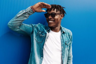 Afrikalı adam güneşe bakıyor, şehirdeki mavi bir binanın arka planında, konsept: başarı için çabalama