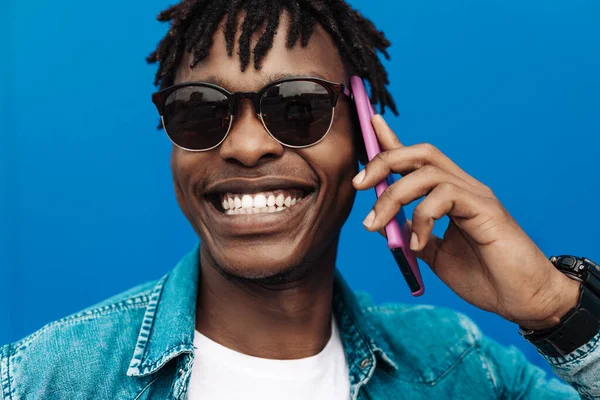 african man calling on the phone on a blue background, 5g internet concept, high speed internet on the phone, black man in blue shirt laughing with a phone in his hands