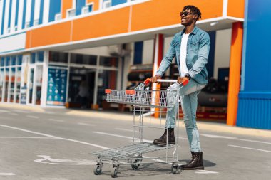 Alışveriş merkezinin önünde alışveriş arabası olan Afro-Amerikan siyah adam, başarılı bir alışveriş merkezi.