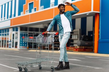 Alışveriş merkezinin önünde alışveriş arabası olan Afro-Amerikan bir adam başarılı bir alışveriş merkezi,