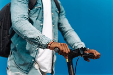 Elektrikli scooter kullanan bir adamın direksiyon simidi mavi bir binanın arka planına karşı açık havada gidiyor.