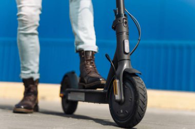 Şehir yolunda, elektrikli scooter kullanan bir adamın yakın çekimi, bacağı bir scooter 'ın üzerinde duruyor.