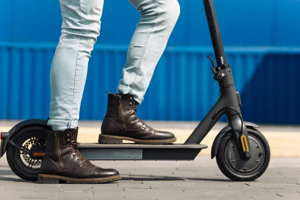 Şehir yolunda, elektrikli scooter kullanan bir adamın yakın çekimi, bacağı bir scooter 'ın üzerinde duruyor.