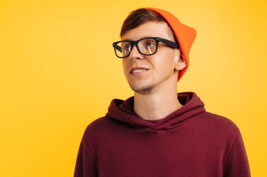 Turuncu şapkalı yakışıklı bir adamın portresi, kırmızı kazak ve gözlüklü, sarı arka planda, geniş gülümsemeli, sonbahar havasında.