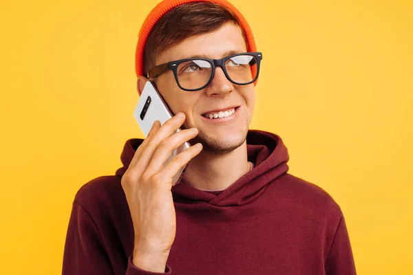 주황색 모자를 스웨터를 잘생긴 전화로 노란색 배경에 웃으며 말한다 — 스톡 사진
