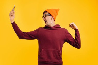 Turuncu şapkalı şık genç adam ve kırmızı kazaklı adam telefondaki mesajla seviniyor, ellerini kaldırmanın başarısını gösteriyor, sonbahar havasında.