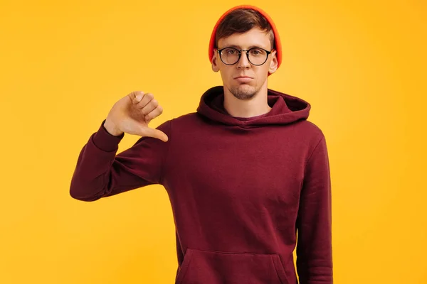 親指を立てる男はオレンジの帽子と赤いセーターに黄色の背景でジェスチャーを嫌う — ストック写真