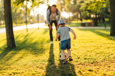 Baba oğul futbol oynuyor, babalar günü, neşeli adam güneşli bir günde parkta çocuklara futbol öğretiyor, aile sporu, hafta sonu sporu.