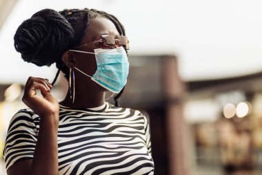Alışveriş merkezinde koruyucu maske takan Afrikalı genç bir kadın alışveriş torbaları, alışveriş konsepti, karantina, COVID-19