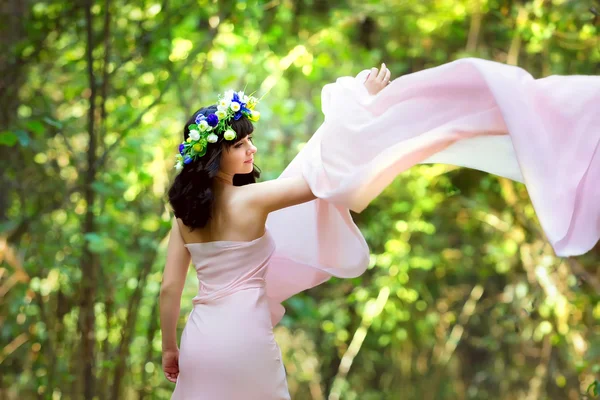 Ragazza molto bella in un abito rosa con i fiori tra i capelli in una radura della foresta — Foto Stock