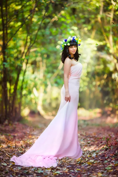 Menina muito bonita em um vestido rosa com flores em seu cabelo em uma clareira florestal Imagens De Bancos De Imagens Sem Royalties