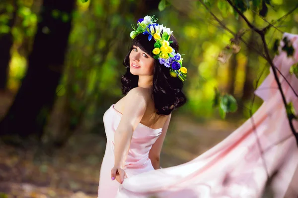Πολύ όμορφο κορίτσι σε ένα ροζ φόρεμα με λουλούδια στα μαλλιά της σε ένα ξέφωτο του δάσους — Φωτογραφία Αρχείου