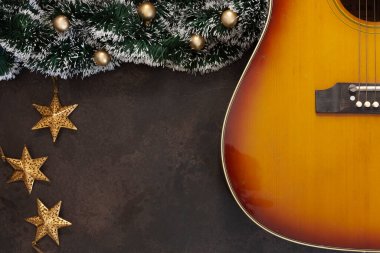 Acoustic guitar and Christmas garland decor with golden Christmas stars on dark brown background	 clipart