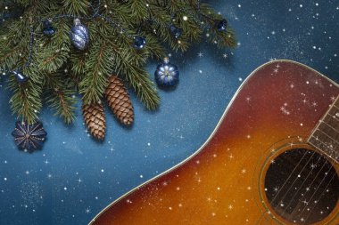 Acoustic guitar and Christmas tree branches with blue dekorative balls on blue background with glitter clipart