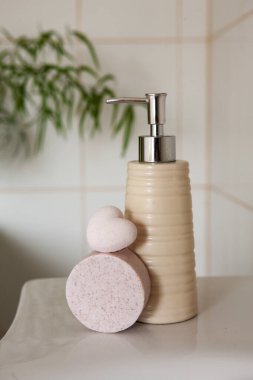Banyo seramik şişesi, sabun ve banyo bombası. Banyo arka planında lavabo var.