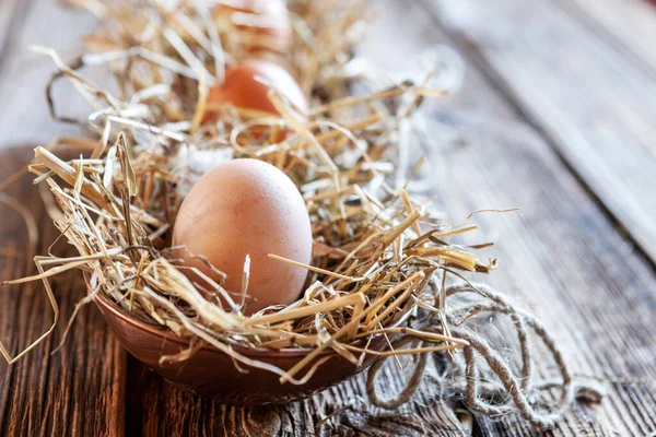 Fresh farming eggs in the nest and feathers in straw on wooden background. Easter decorating, Selective focus