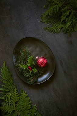 Noel tatili arka planında köknar ağacı ve çoban püskülü dalları, koyu arkaplanda kırmızı top