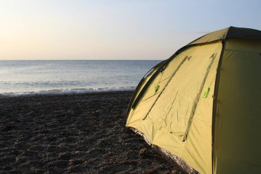 Yazın güneşli bir sabahta kumsalda yeşil turist çadırı turistler için fotoğraf çadırı. Deniz kıyısında duruyor. Sabah güneşli, yılın zamanı yaz, sonbahar. Karadeniz kıyısındaki kumsal.
