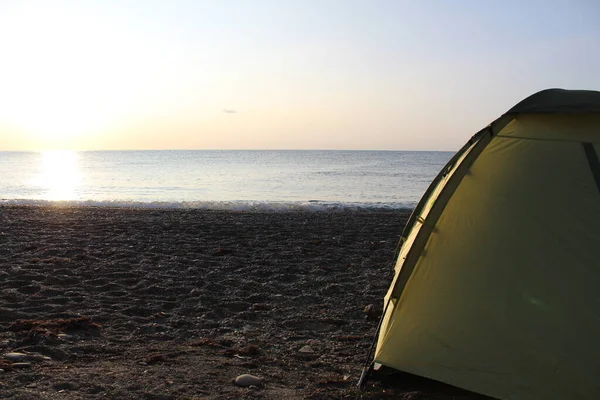 green tourist tent on the beach on a Sunny morning in summer / photo tent for tourists. it stands on the seashore.the morning is Sunny, the time of year is summer, autumn. beach on the Black sea.