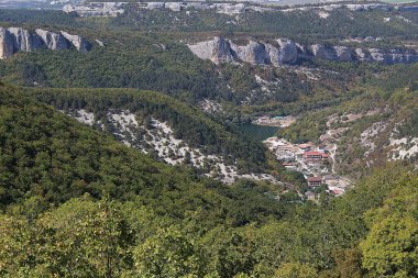 Vadi manzarası, göl ve Mangup-Kale köyü Kırım 'daki dağlardan / fotoğraf dağ manzarası. Köy dağların arasında yer almaktadır. Kızıl çatılı evler. Gölün ortasında. Dağlar ormanla kaplı.. 