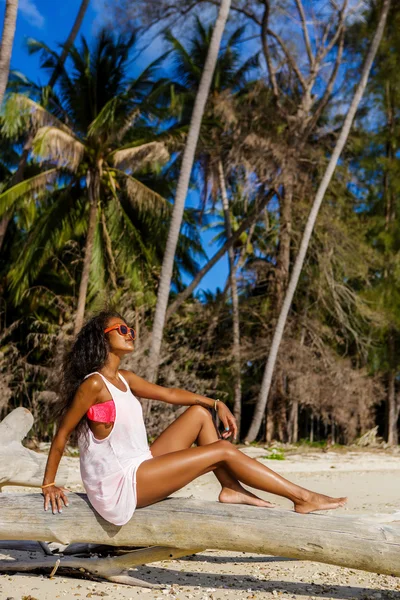 Mooie zwarte tienermeisje zitten op palmboom op het strand. — Stockfoto