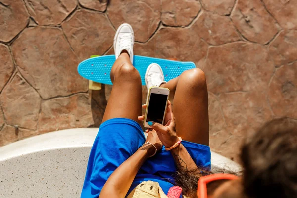 Красивая девушка-подросток в голубой юбке сидит со своим смартфоном — стоковое фото