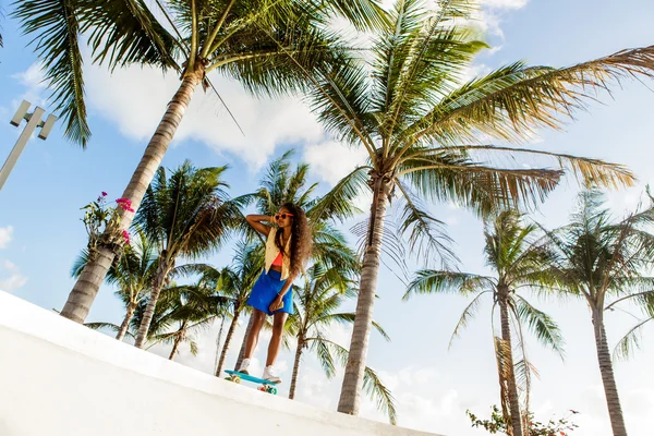 Vacker svart tonårsflicka i ljusa outfit rider på tropical — Stockfoto