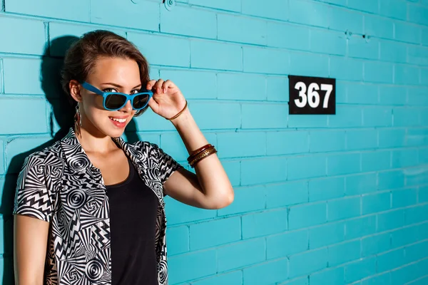 Heureuse jeune fille dans les lunettes de soleil avoir du plaisir en face de brique bleue — Photo