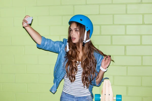 Bella ragazza dai capelli lunghi con uno smartpnone vicino a un mattone verde — Foto Stock