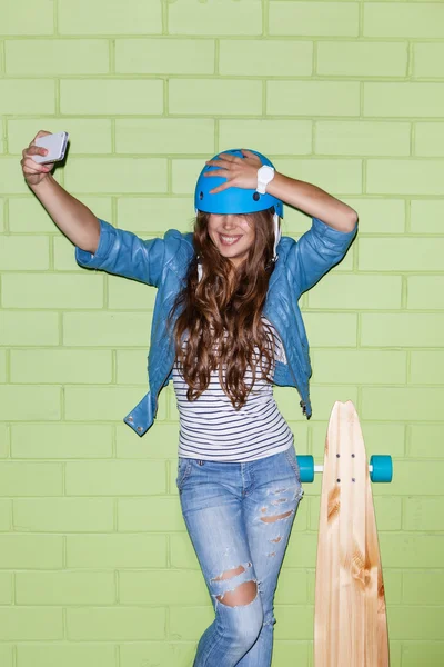 Bella ragazza dai capelli lunghi con uno smartphone vicino a un mattone verde — Foto Stock