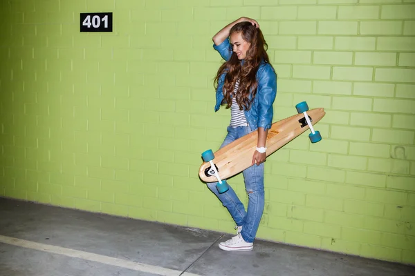 Bela senhora de cabelos longos com um skate longo de madeira perto de um — Fotografia de Stock
