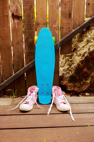 Sapatilhas rosa converse perto de patins azuis que fica perto de madeira — Fotografia de Stock