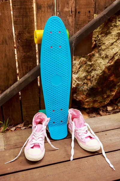 Pink converse sneakers near blue skate which stands near wooden