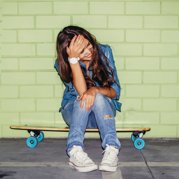 Bela senhora de cabelos longos com um skate de madeira perto de um verde — Fotografia de Stock