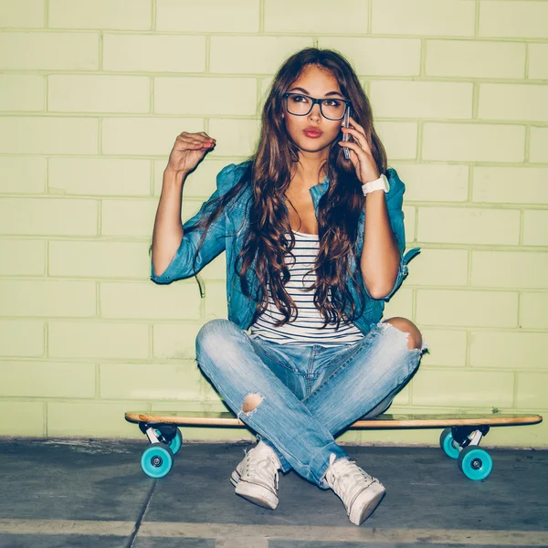 Girl sits on skateboard talking on smartphone — Zdjęcie stockowe