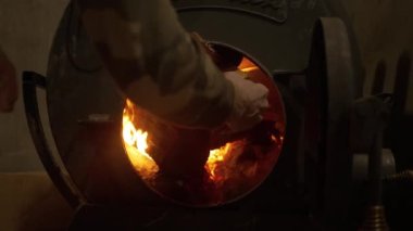 Bir adam odunları ahşap bir evdeki demir sobaya koyar. Kış