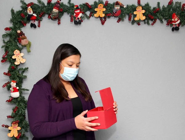 black hair latin woman with protection mask and gift box in christmas decoration, new normal covid-19