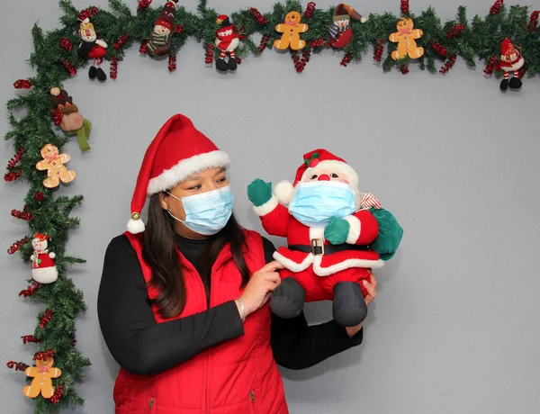 Latin woman with protection mask, hat and Santa Claus doll in Christmas decoration, new normal covid-19