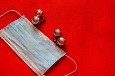 Kırmızı arka planda koruma maskesi olan gümüş noel yıldızı ve küreler, yeni normal covid-19 noeli.