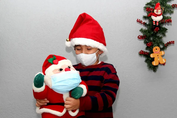 7 yaşında Latin bir çocuk ve koruyucu maskeli Noel Baba, gri arka planda noel süslemesi, yeni normal covid-19